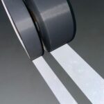 dois rolos de fita refletiva 50 ciclos, um com 5 cm de largura e outro com 2,5 cm de largura, localizados em um ambiente escuro com incidência de luz para exibir a refletividade