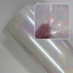 Rolo de foil furta-cor com efeito mancha de óleo, refletindo tons suaves de rosa, verde e amarelo perolado. No destaque, uma mão mostra a transparência e a leveza do material.