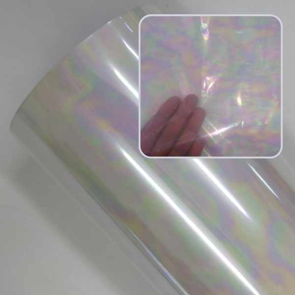 Rolo de foil furta-cor com efeito mancha de óleo, refletindo tons suaves de rosa, verde e amarelo perolado. No destaque, uma mão mostra a transparência e a leveza do material.